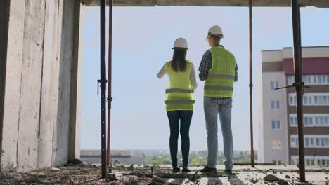 back view young foreman and engineer checking the blueprint and talking about construction project with commitment to success at construction site