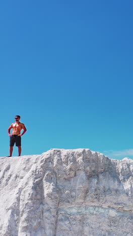 sportsman standing on cliff of mountain. man with naked torso standing on top of mountain and enjoying nature. vertical video
