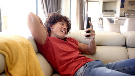 a young biracial man lounges on a sofa at home, smartphone in hand