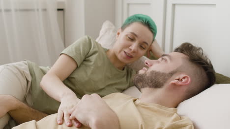 happy young couple holding hands and talking together while lying on the bed 1