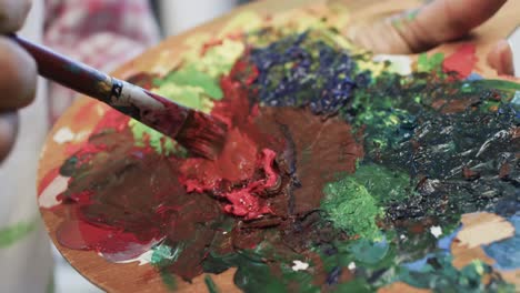 Hands-of-biracial-female-artist-in-apron-mixing-paints-on-palette-using-brush-in-studio,-slow-motion