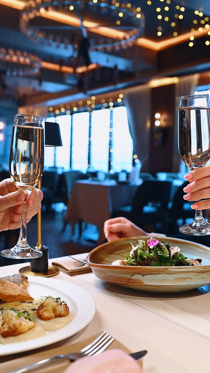 Cena celebrativa con bevande e cibo in un ristorante di sera. Due persone si godono un pasto al ristorante, alzando i bicchieri per un brindisi con del cibo sul tavolo.