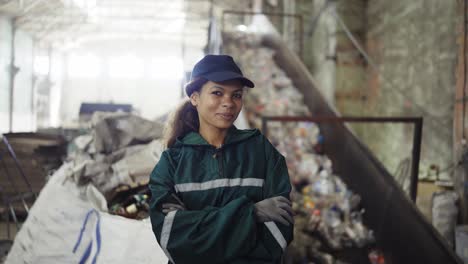 portrait of a young african-american woman checks a conveyor belt at a recycling plant. pollution control