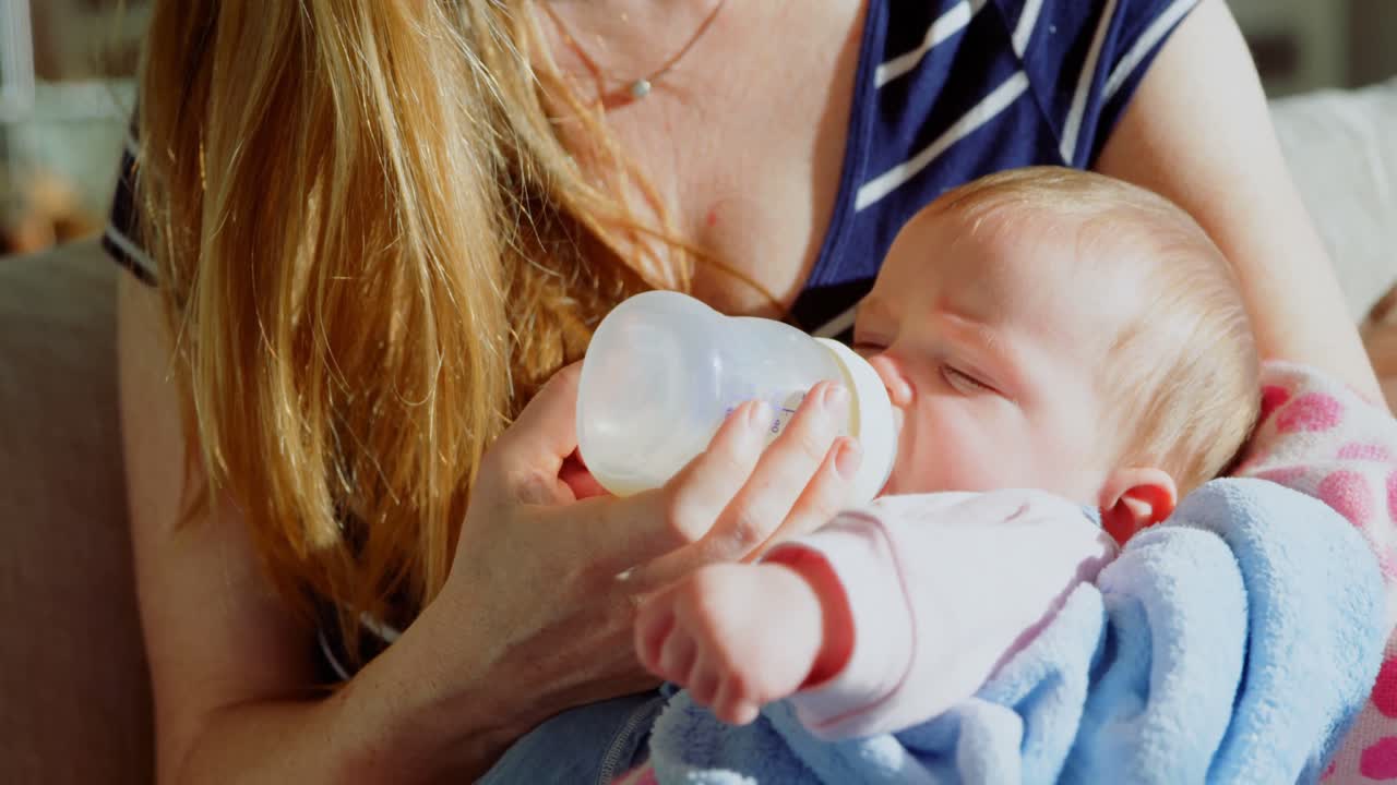 primer plano de una madre caucásica adulta alimentando a su bebé con leche del biberón en un hogar cómodo 4k