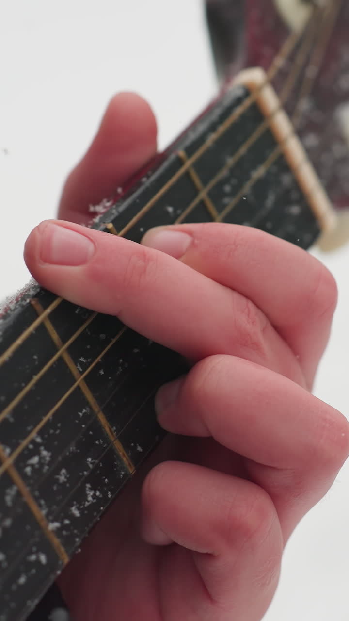 Close-up of hand playing guitar on snow-covered strings, creating a perfect harmony between music and winter's serene beauty, with frosty textures on black sleeve and guitar neck