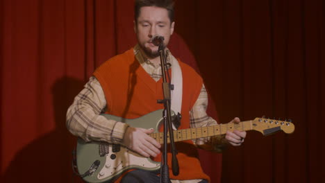 concentrated male musician with guitar and microphone sitting on stool and getting ready for a live performance 1