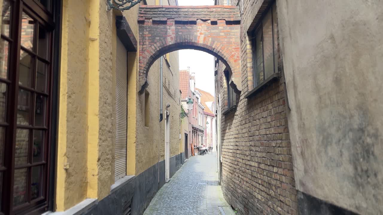 Vista tranquilla di una stretta strada acciottolata con vecchie mura di mattoni e arco nella città di Bruges