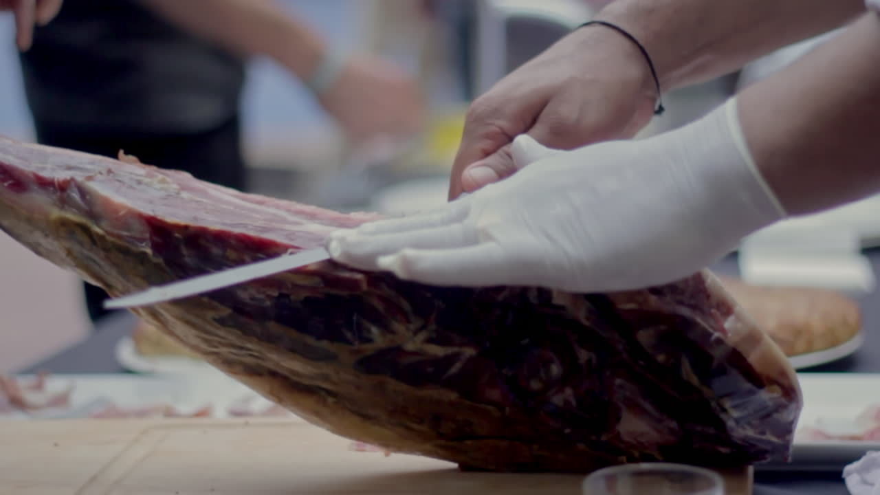 A gloved hand expertly slices cured ham during a gourmet food presentation