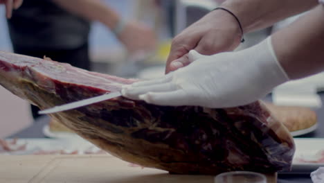 a gloved hand expertly slices cured ham during a gourmet food presentation