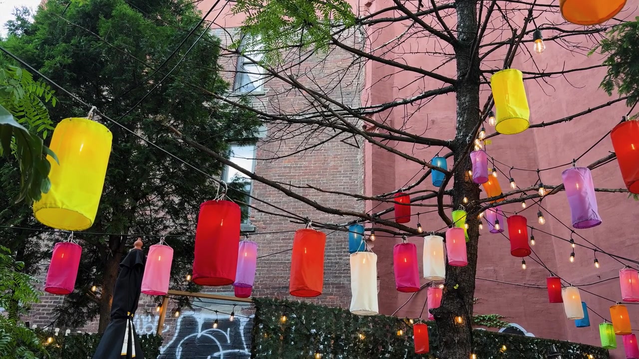 都会の屋外中庭で、色鮮やかなランタンが木の枝からぶら下がっている情景