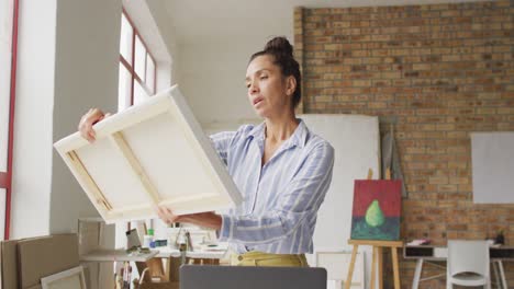 video of happy biracial female artist looking at painting in studio