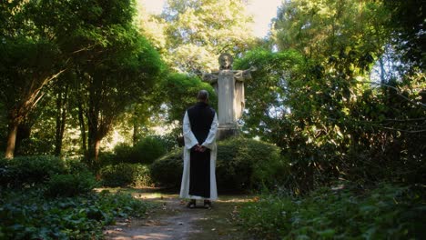 increíble escena de un monje rezando en una estatua de jesús rodeada de hermosa naturaleza y árboles