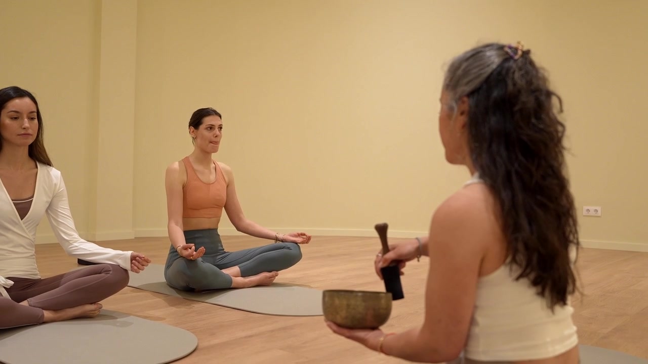 Istruttore di yoga che suona una campana tibetana per donne in meditazione
