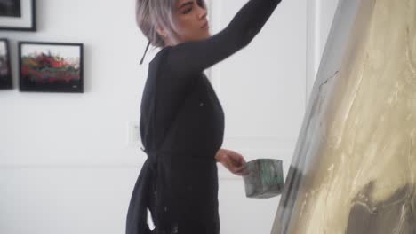 latina artist working with large paintbrush standing in front of wide canvas