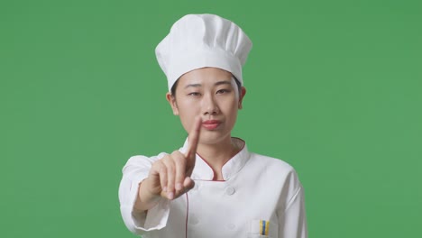 close up of asian woman chef pointing at you and disapproving with no index finger sign in the green screen background studio