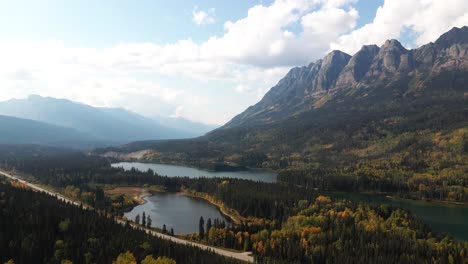 awe-inspiring-aerial-pan-zoom-shot-of-Mount-Robson-Provincial-Park-in-the-autumn-at-yellowhead-lake-on-a-mix-of-sun-and-cloud-day-with-Yellowhead-Highway-in-front-and-colorful-trees