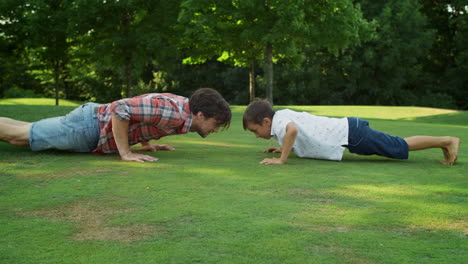 Boy-and-man-standing-in-plank-position.-Father-and-son-doing-push-ups-in-park