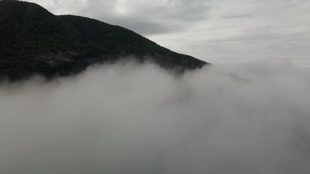 두꺼운 흰 구름이 캐나다 퀘벡의 개스페 반도 옆에 있는 세련된 산과 마을을 덮었습니다.