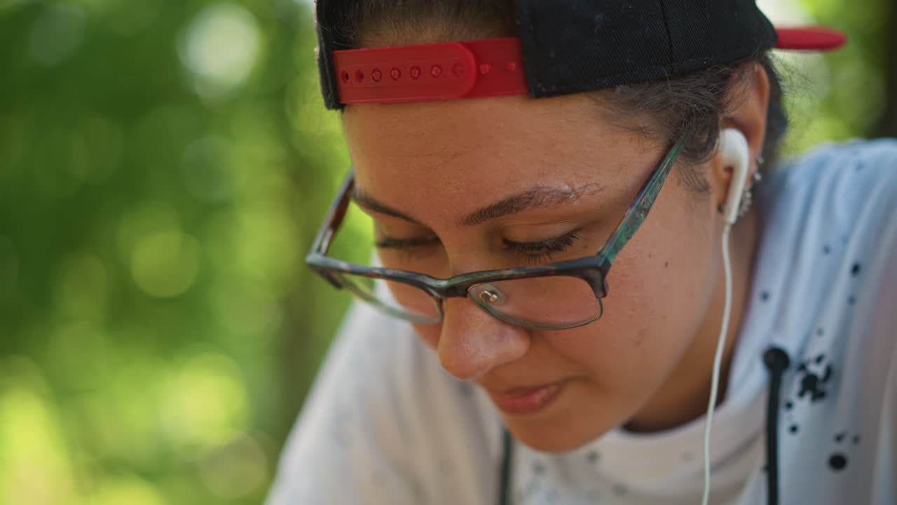adolescente birracial estudiando al aire libre con auriculares, poeta tomando notas en un banco del parque, artista dibujando hojas bajo los árboles, programador revisando líneas en el teléfono, investigador de campo leyendo datos, escritor practicando