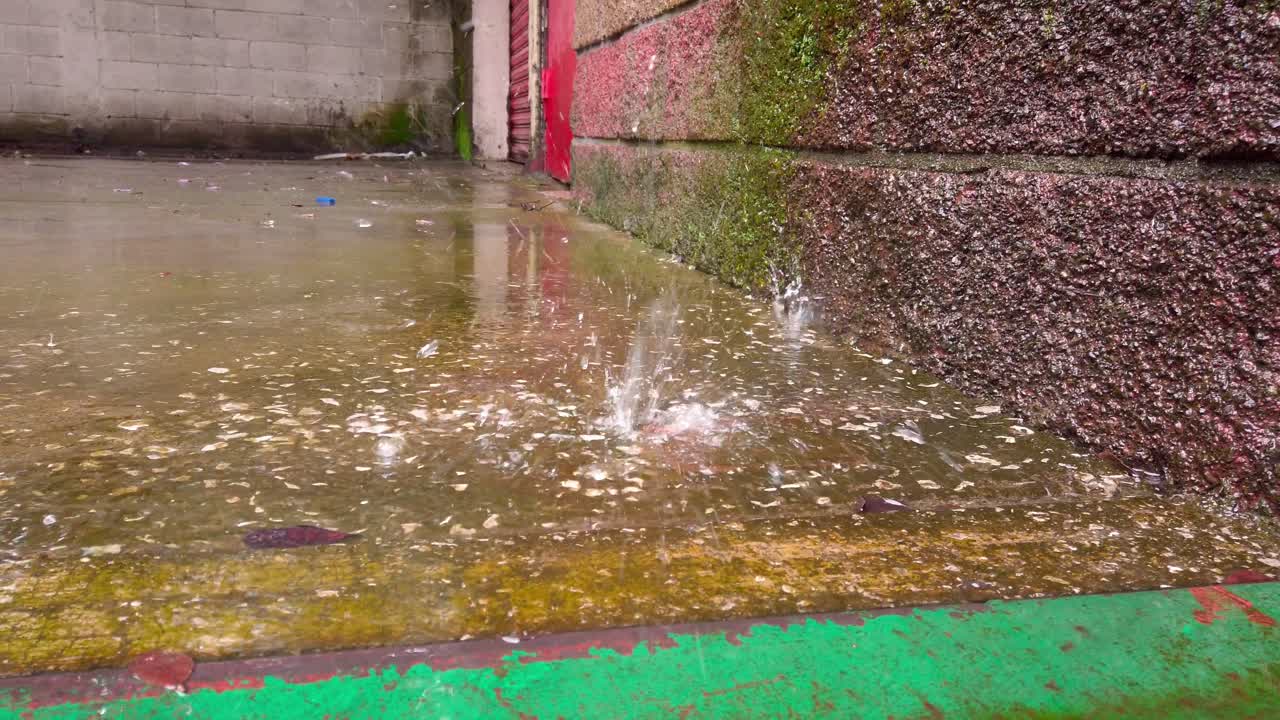 Close-up of rain hitting wet concrete surface creating splash in urban setting.