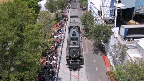 steam train passing through city, large crowd watching