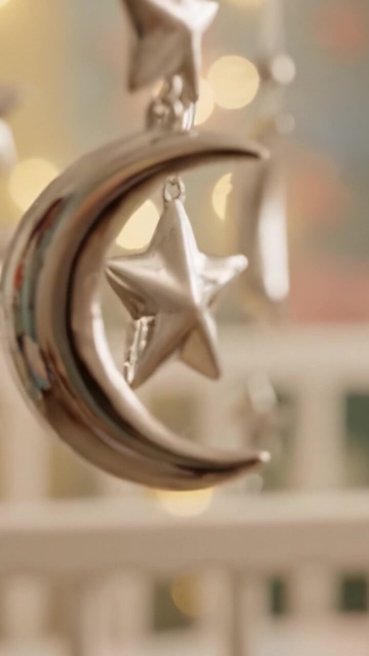 A Dreamy Mobile Display Featuring Silver Stars and Moons Illuminated by Soft Bokeh Lights for a Baby's Nursery Decor