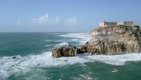 las olas del océano golpean los acantilados del fuerte de sao miguel arcanjo en un día soleado en nazare, portugal