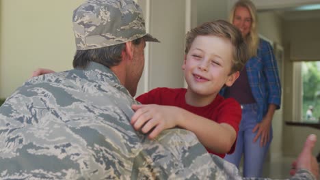 Kaukasischer-Männlicher-Soldat-Umarmt-Seinen-Lächelnden-Sohn-über-Lächelnder-Frau-Und-Amerikanischer-Flagge