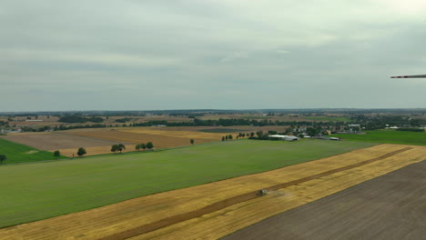 aerial view of a tractor working in a wheat field surrounded by green fields and wind turbines. the highlights harmony between agriculture and renewable energy