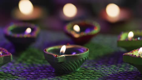 Lit-candles-in-decorative-clay-pots-on-woven-table-mat,-focus-on-foreground,-bokeh-background