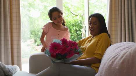 hija dando a la madre un ramo de flores y una tarjeta casera para el cumpleaños o el día de la madre en casa