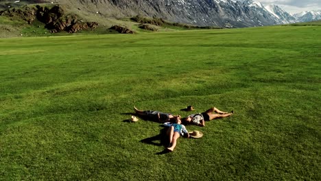 three attractive girls lying on green grass and having fun on a meadow sunny day and background of mountain