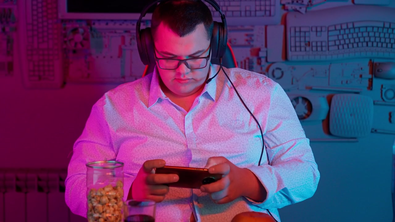 Giovane uomo concentrato che gioca a un gioco mobile in una stanza illuminata al neon