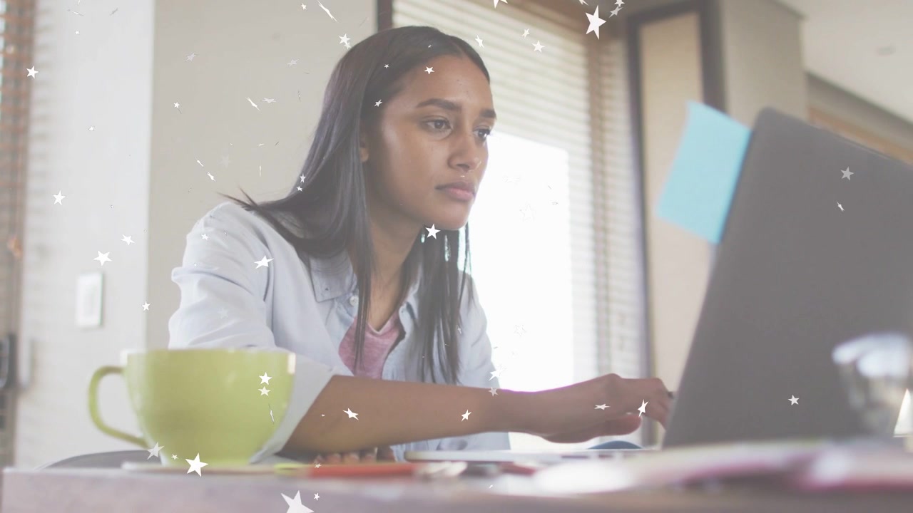 Mulher sentada à mesa digitando no laptop, ativando sobreposições de estrelas enquanto consulta anotações para estudo