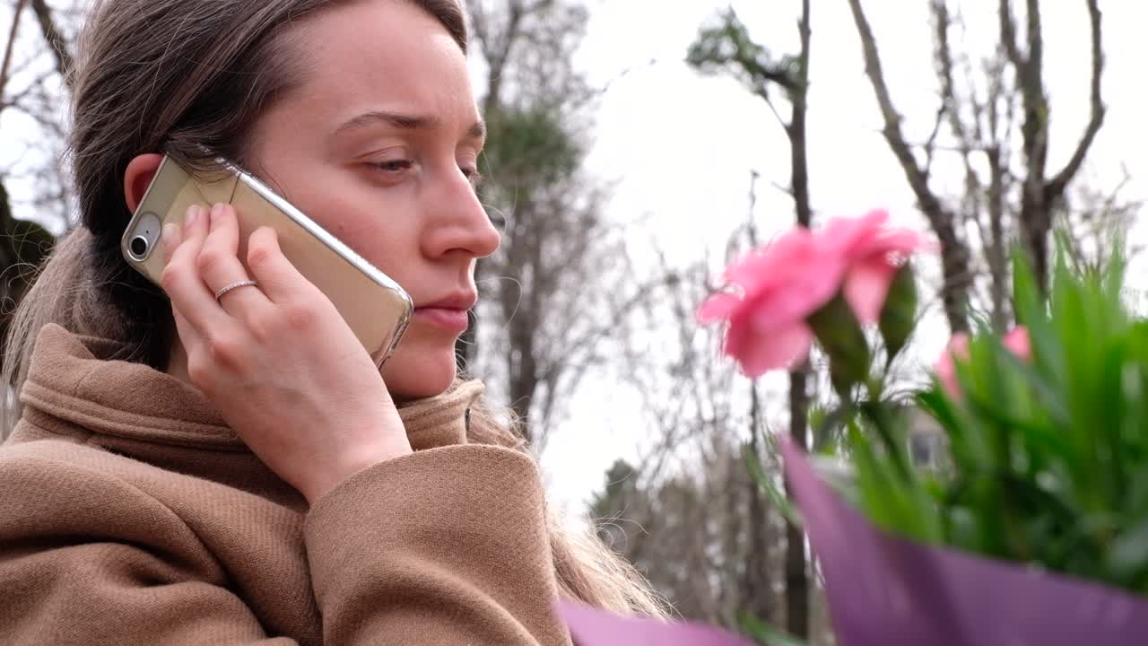 Brunette woman wearing a brown coat talking on the phone at a terrace