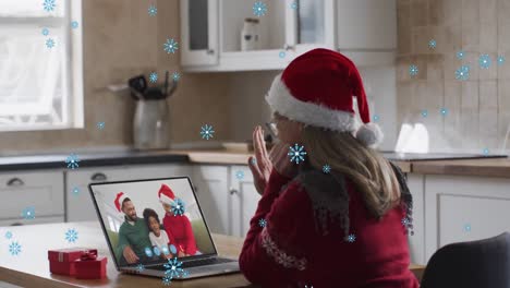 Animation-of-snow-falling-over-happy-caucasian-woman-in-santa-hat-on-laptop-video-call