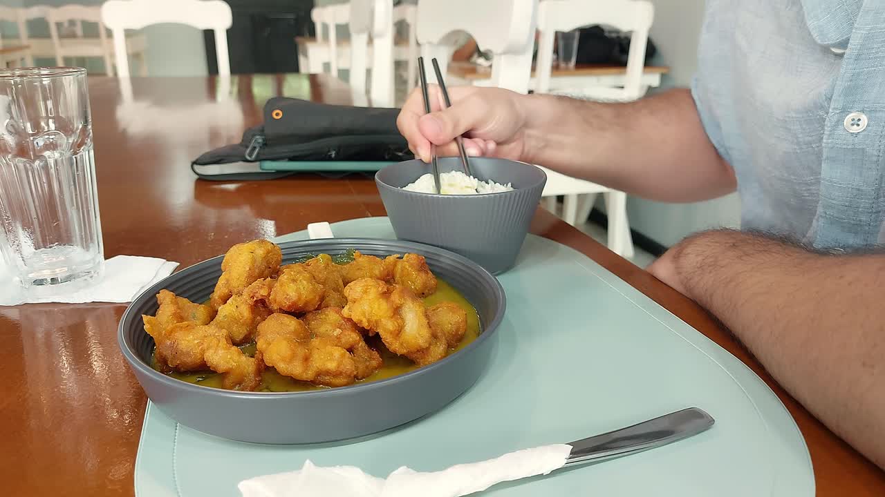Man eating a plate of Korean popcorn chicken nugget called Dakgangjeong in curry sauce with rice using metal chopstick, traditional authentic korean dish