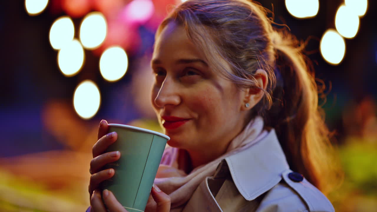 Donna che beve una bevanda calda in una strada illuminata di sera