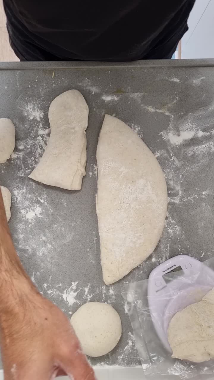 Preparazione dell'impasto napoletano: mani usano una spatola di metallo per porzionare un lungo cilindro di impasto per pizza a lunga fermentazione. Video verticale
