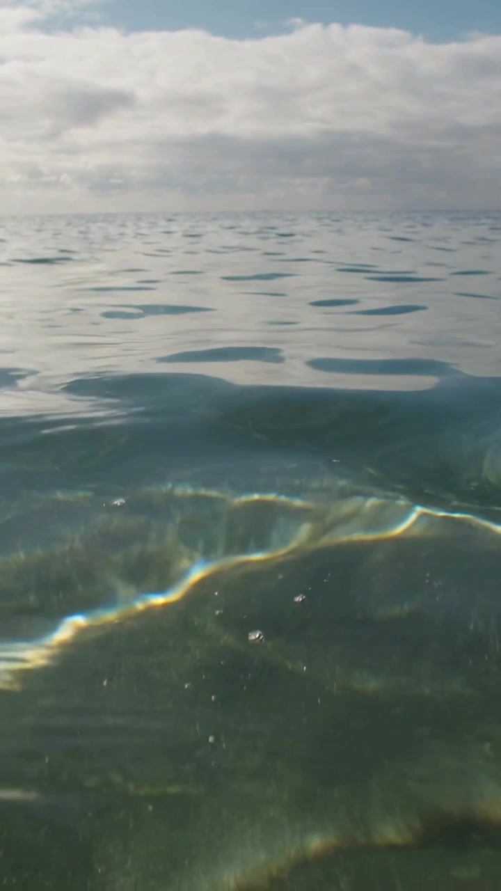Vertical video: Rolling sea surface riding swell, showing caustic light at lens, bubbles drifting