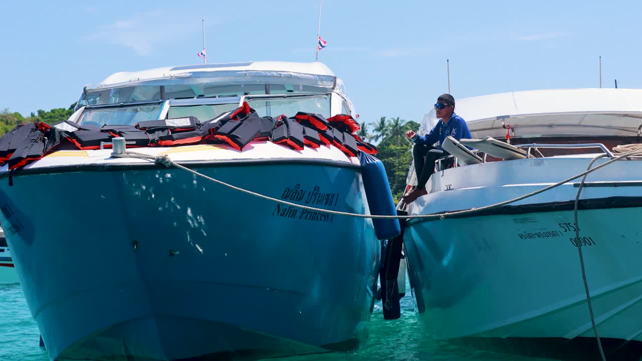 Two boats maneuver in turquoise waters near a rocky shoreline under bright daylight, showcasing nautical activity in Phuket