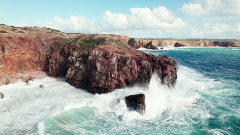 Aerial-4k-drone-reverse-view-of-large-crashing-waves-at-Praia-da-Zimbreirinha-hidden-cliff-coastline-near-Bordeira-in-the-Algarve-region-of-Portugal