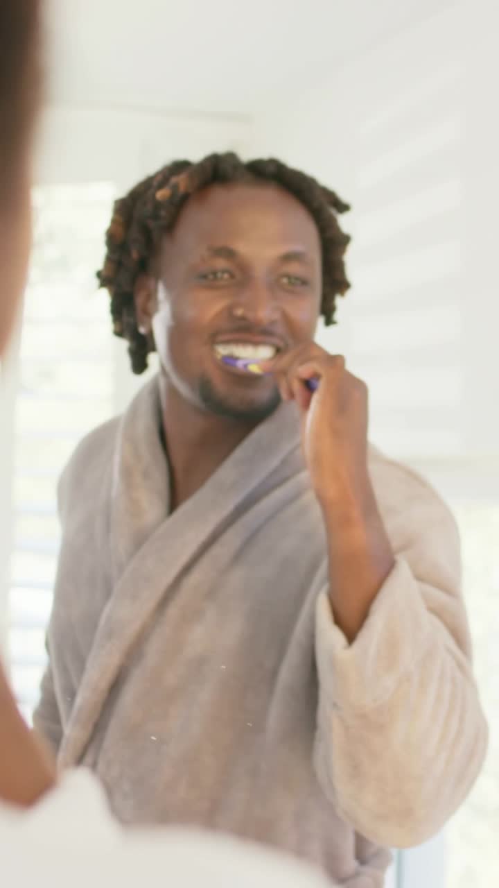 Vertical video: Lifting toothbrush, man in bathrobe brushing teeth at bathroom mirror for work