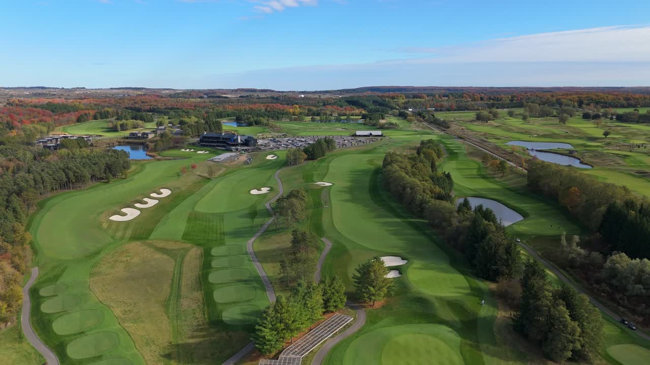 A stunning aerial view of the TPC Toronto at Osprey Valley golf course, showcasing the immaculate, rolling fairways and pristine white sand bunkers, all framed by vibrant autumn colours