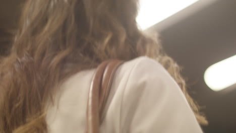 joven hermosa y elegante mujer con cabello marrón camina bajo luces gigantes en la plataforma del metro subterráneo en cámara lenta y poca profundidad de campo