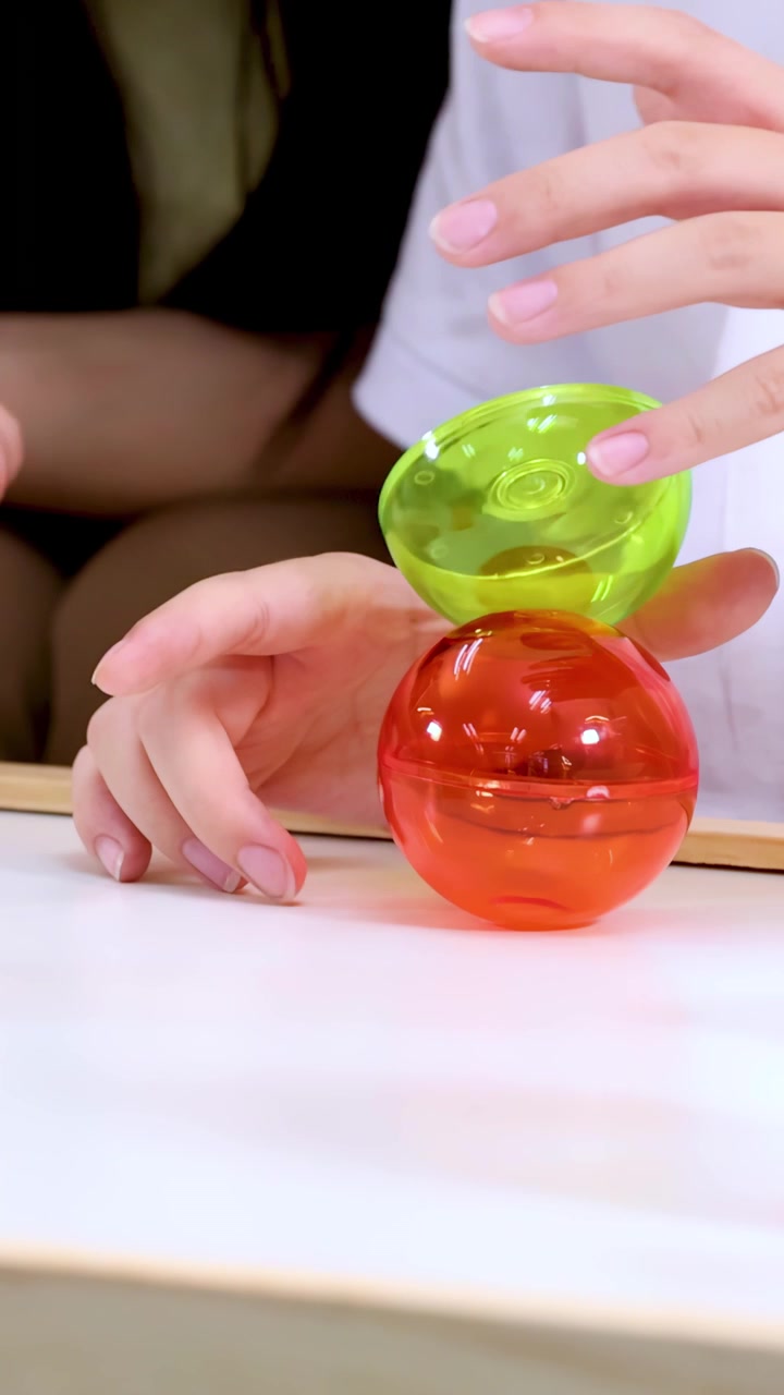 Close-up of child hands stacking translucent toy spheres on bright classroom table, soft lighting