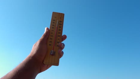 hand holding thermometer against a blue sky