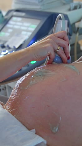 pregnant woman in mask lies on the doctor's couch. doctor moves the equipment around the belly with gel. close up. vertical video