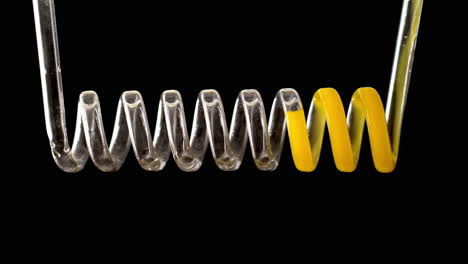 the yellow liquid fills the spiral of glass on a black background in slow motion. chemical capacitor on a black background. high quality 4k footage