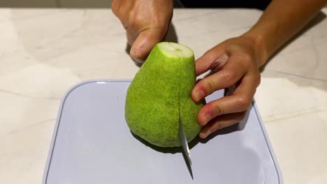 person slicing a pear on cutting board